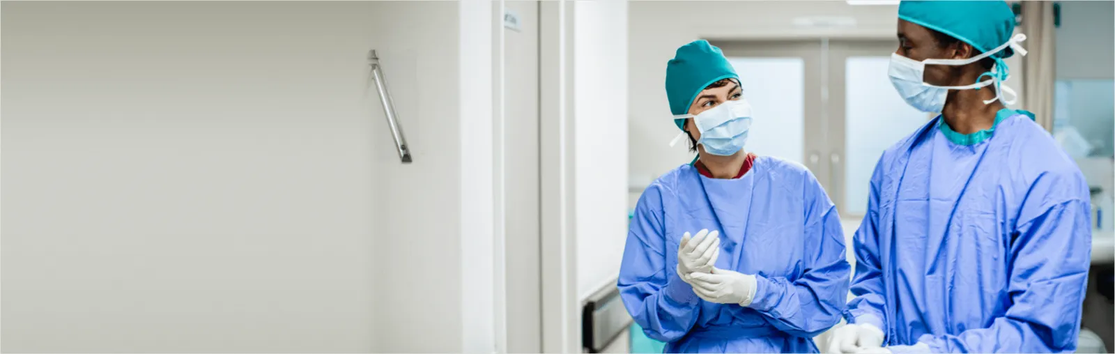 Two healthcare workers wearing hair coverings, face masks, blue protective clothing and gloves